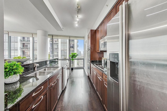 kitchen with appliances with stainless steel finishes, dark stone counters, sink, a wall of windows, and dark hardwood / wood-style floors