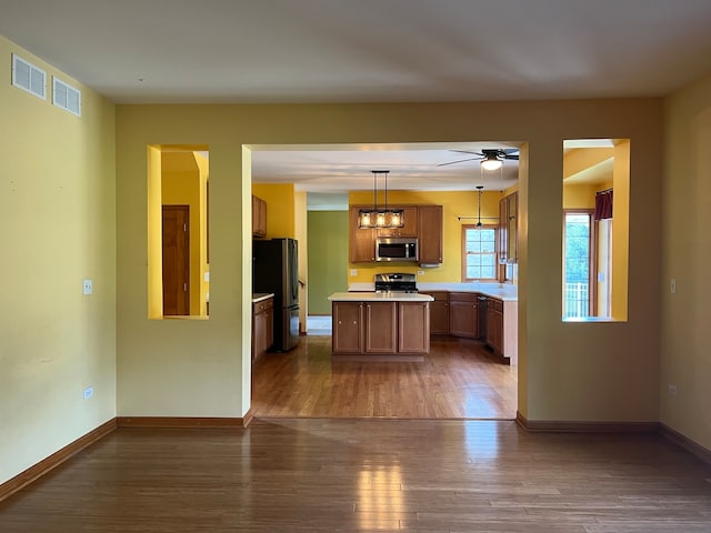 kitchen featuring a kitchen island, appliances with stainless steel finishes, hanging light fixtures, dark wood-type flooring, and ceiling fan