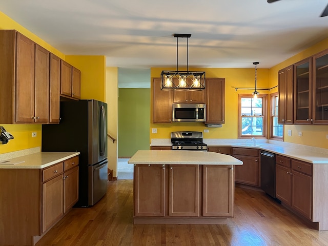 kitchen with wood-type flooring, light stone counters, appliances with stainless steel finishes, decorative light fixtures, and a center island