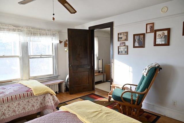 bedroom featuring ceiling fan, radiator heating unit, and light wood-type flooring