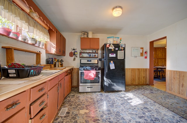 kitchen with black refrigerator, wood walls, and gas range