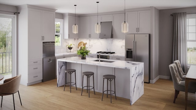 kitchen featuring ventilation hood, a center island with sink, decorative backsplash, light wood-type flooring, and appliances with stainless steel finishes