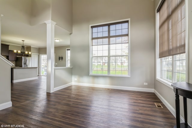 unfurnished living room with decorative columns, crown molding, a chandelier, and dark hardwood / wood-style floors