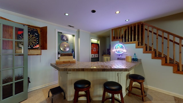 bar featuring light tile patterned floors, tile counters, and ornamental molding