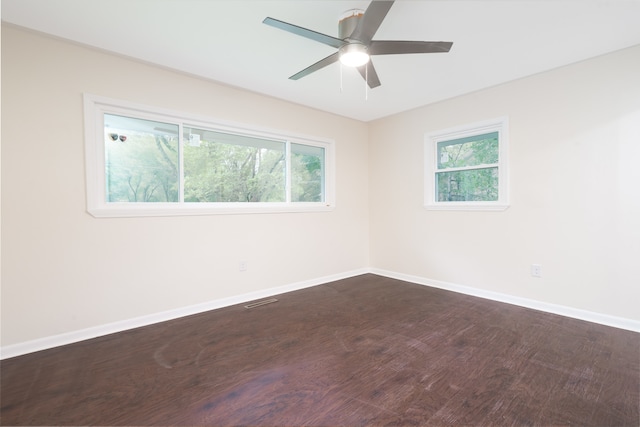 empty room with a wealth of natural light, dark wood-type flooring, and ceiling fan