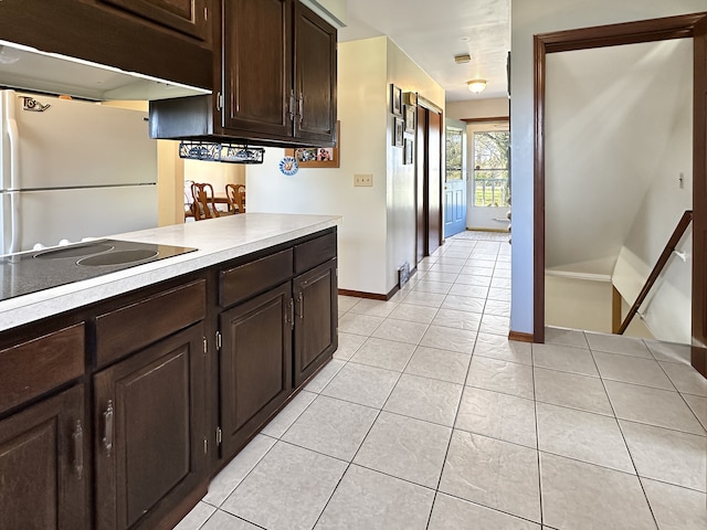 kitchen with stainless steel refrigerator, dark brown cabinetry, light tile patterned floors, and black electric cooktop