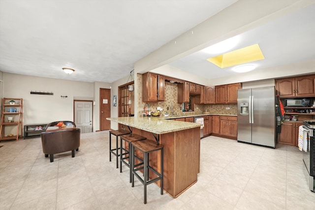 kitchen with light stone countertops, kitchen peninsula, decorative backsplash, a breakfast bar, and appliances with stainless steel finishes