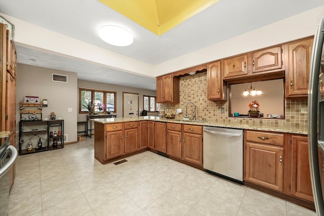 kitchen with kitchen peninsula, decorative backsplash, light stone counters, stainless steel dishwasher, and sink