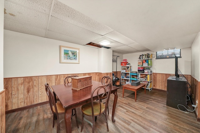 dining room featuring wood walls, hardwood / wood-style floors, and a drop ceiling