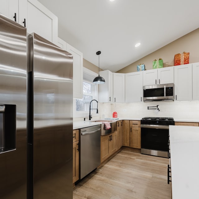 kitchen with decorative backsplash, appliances with stainless steel finishes, decorative light fixtures, white cabinets, and light hardwood / wood-style floors