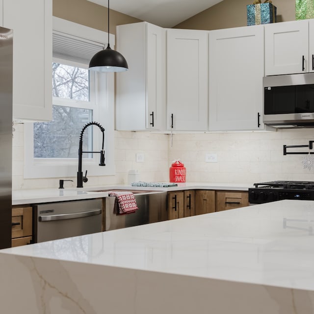 kitchen with light stone countertops, hanging light fixtures, stainless steel appliances, backsplash, and white cabinets