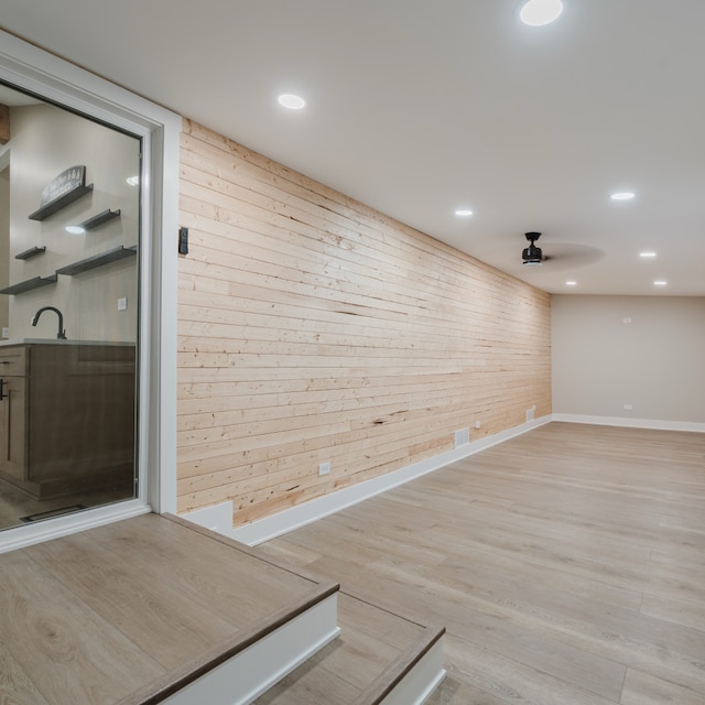 empty room with light hardwood / wood-style flooring, ceiling fan, wooden walls, and sink