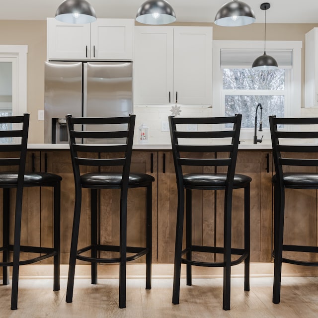 kitchen with a kitchen breakfast bar, sink, white cabinetry, and stainless steel refrigerator with ice dispenser