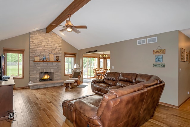 living room featuring lofted ceiling with beams, light wood-type flooring, a fireplace, and ceiling fan with notable chandelier