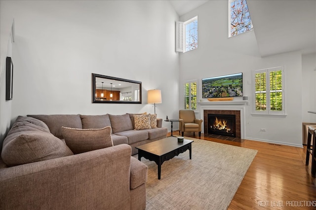 living room with light wood-type flooring, a towering ceiling, and a tile fireplace