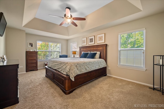 carpeted bedroom featuring ceiling fan, a tray ceiling, and multiple windows