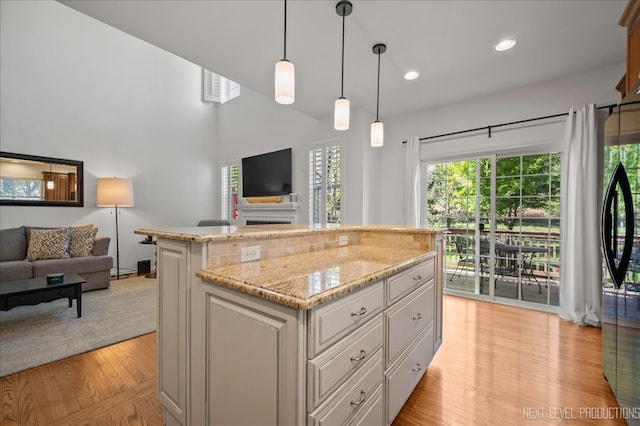 kitchen with pendant lighting, a kitchen island, light stone counters, and light hardwood / wood-style flooring