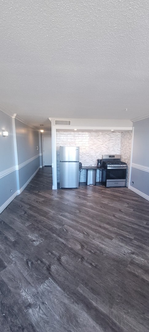 unfurnished living room featuring dark wood-type flooring, a textured ceiling, and crown molding