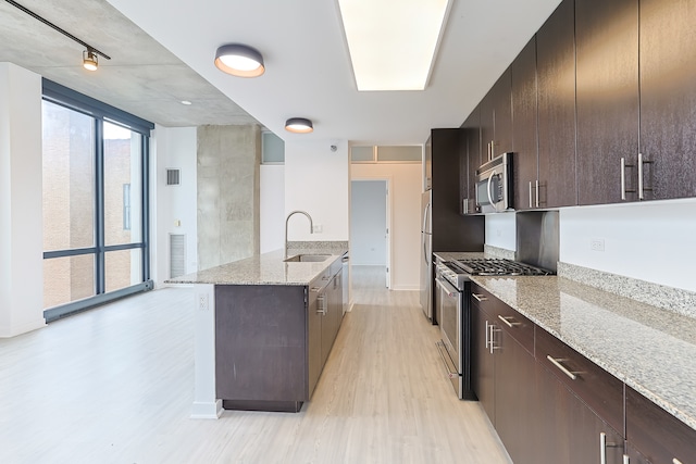 kitchen with stainless steel appliances, light stone counters, sink, a kitchen island with sink, and light wood-type flooring