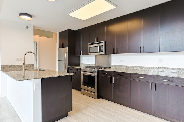 kitchen featuring dark brown cabinetry, light hardwood / wood-style flooring, sink, light stone countertops, and appliances with stainless steel finishes