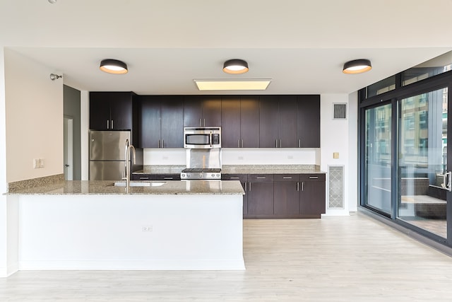 kitchen with stainless steel appliances, light stone countertops, sink, light hardwood / wood-style floors, and kitchen peninsula