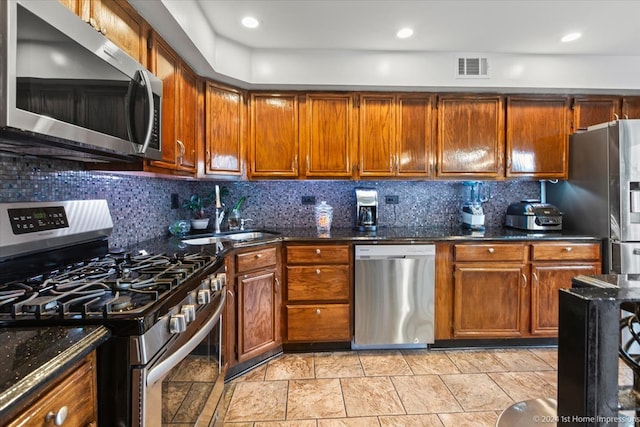 kitchen with decorative backsplash, appliances with stainless steel finishes, sink, and dark stone countertops