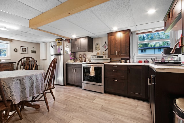 kitchen featuring light wood-type flooring, appliances with stainless steel finishes, a drop ceiling, and dark brown cabinets