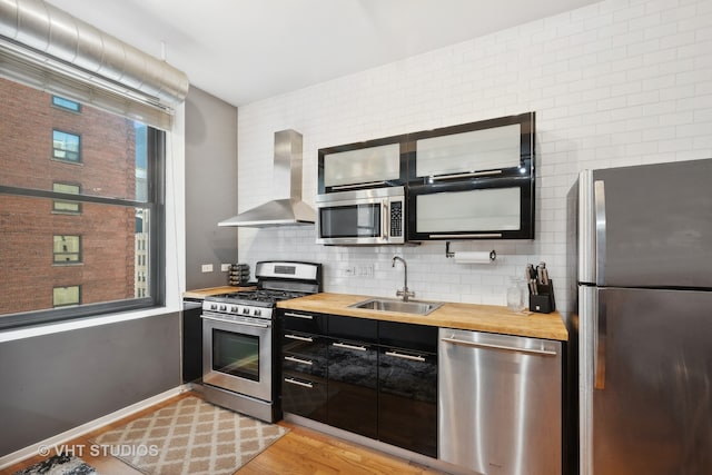 kitchen featuring wall chimney range hood, appliances with stainless steel finishes, wood counters, sink, and light hardwood / wood-style floors