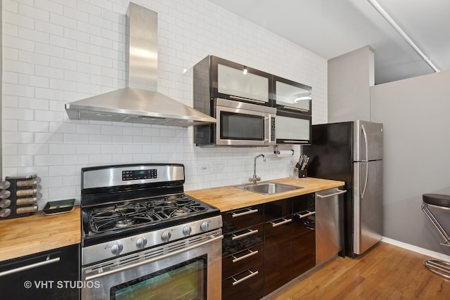 kitchen with light wood-type flooring, appliances with stainless steel finishes, wood counters, sink, and wall chimney exhaust hood