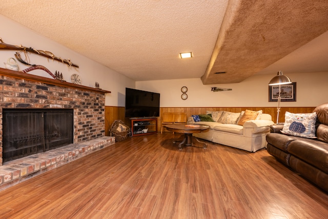 living room featuring hardwood / wood-style floors, wood walls, a textured ceiling, and a brick fireplace