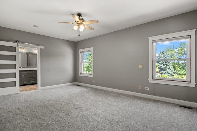 unfurnished bedroom featuring a barn door, light carpet, ceiling fan, and ensuite bathroom