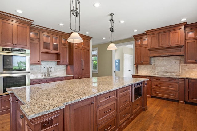 kitchen featuring appliances with stainless steel finishes, light stone countertops, dark hardwood / wood-style floors, decorative light fixtures, and a kitchen island