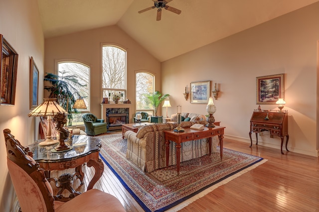 living room featuring ceiling fan, light wood-type flooring, a fireplace, and high vaulted ceiling