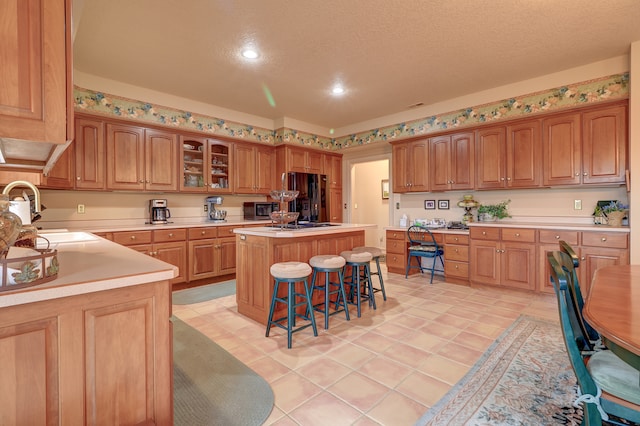 kitchen featuring black refrigerator, a kitchen breakfast bar, a textured ceiling, sink, and a kitchen island