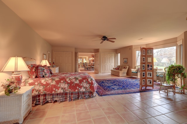 tiled bedroom with ceiling fan and multiple closets