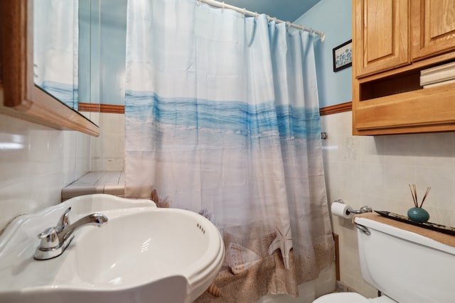 bathroom with a shower with shower curtain, toilet, sink, and tile walls