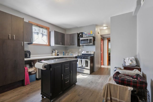 kitchen with light wood-style flooring, a sink, a center island, stainless steel appliances, and light countertops