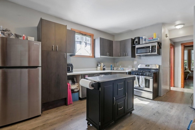 kitchen with a sink, light countertops, light wood-style floors, appliances with stainless steel finishes, and a center island