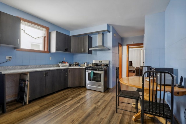 kitchen with stainless steel range with gas cooktop, light countertops, decorative backsplash, wall chimney exhaust hood, and dark wood-style flooring