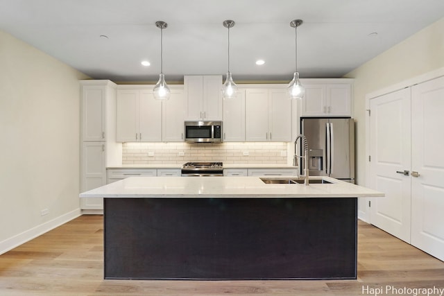 kitchen featuring stainless steel appliances, decorative light fixtures, sink, white cabinets, and a kitchen island with sink