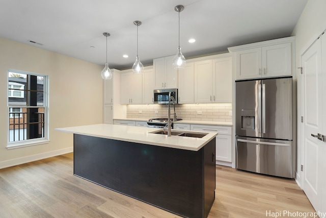 kitchen featuring white cabinets, stainless steel appliances, pendant lighting, and an island with sink