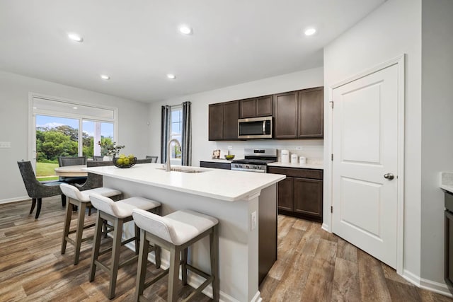 kitchen with a kitchen breakfast bar, sink, hardwood / wood-style flooring, an island with sink, and appliances with stainless steel finishes