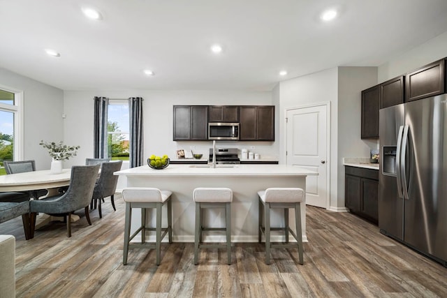 kitchen with dark brown cabinetry, dark hardwood / wood-style flooring, stainless steel appliances, and a kitchen island with sink