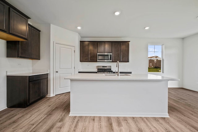 kitchen with an island with sink, appliances with stainless steel finishes, and light hardwood / wood-style flooring