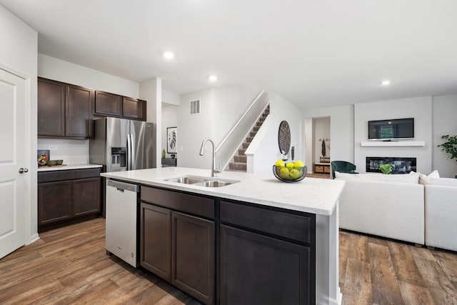 kitchen featuring dark brown cabinetry, sink, dark wood-type flooring, an island with sink, and appliances with stainless steel finishes