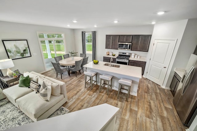 kitchen featuring dark brown cabinetry, a kitchen bar, a center island with sink, appliances with stainless steel finishes, and light wood-type flooring