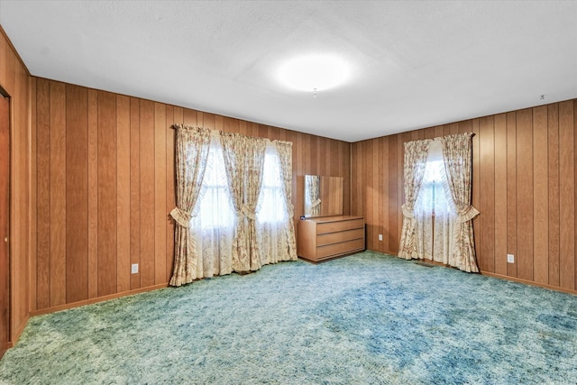 spare room with a textured ceiling, light colored carpet, and wood walls