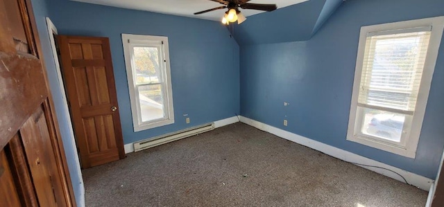 additional living space featuring dark carpet, ceiling fan, a healthy amount of sunlight, and a baseboard heating unit