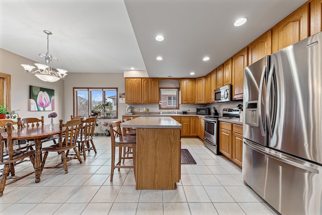 kitchen with hanging light fixtures, light tile patterned floors, appliances with stainless steel finishes, a notable chandelier, and a kitchen island