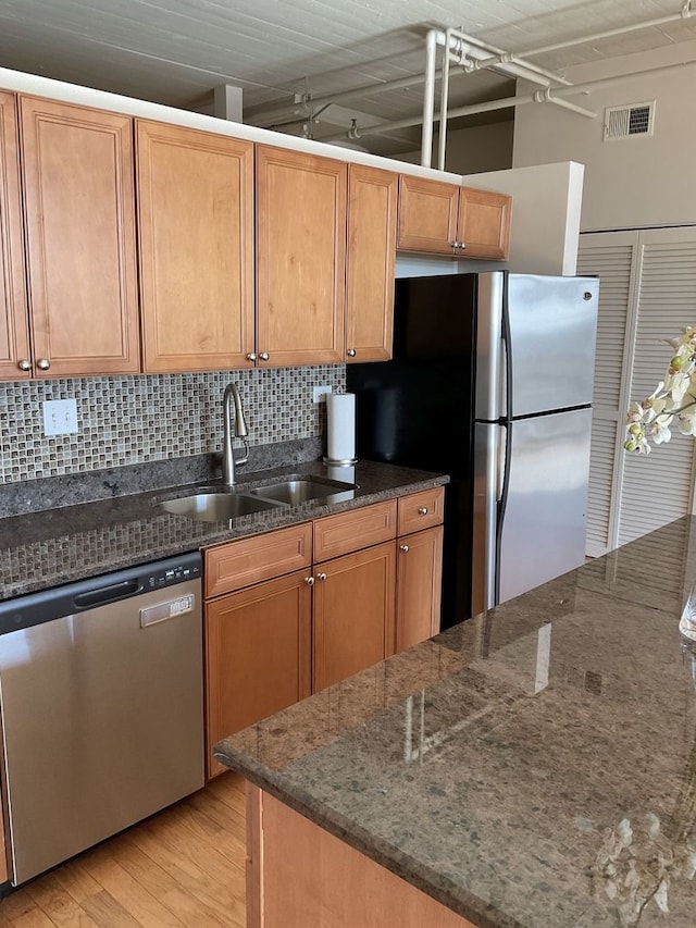 kitchen with appliances with stainless steel finishes, backsplash, sink, dark stone countertops, and light hardwood / wood-style floors